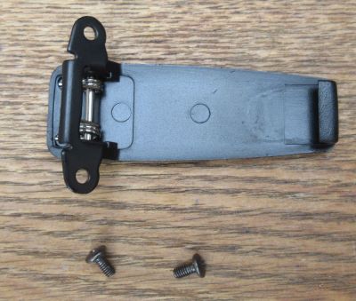amherst-a66-belt-clip-kit Belt Clip for A66 Walkie Talkie Battery is shown on a wooden surface, with two loose screws placed beneath it.
