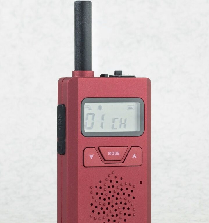 cp183-red-front-view The CPS Telecom CP183 Tiny PMR446 Radio is a red handheld two-way device with a digital "01 CH" display and mode/navigation buttons, standing upright on a light surface.