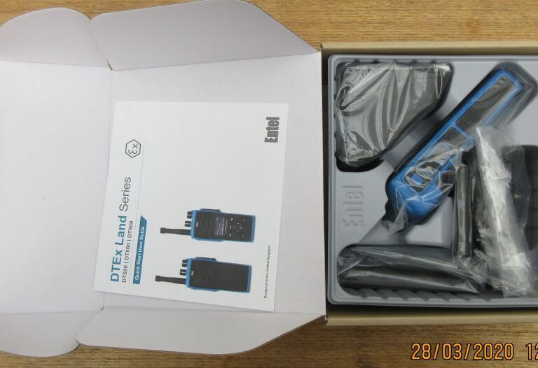 An open box containing an Entel DT982 Atex 2c walkie-talkie set with the radio, aerial, charger, user manual, and accessories neatly packed inside.