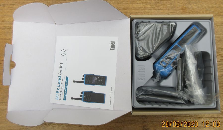 An open box containing an Entel DT982 Atex 2c walkie-talkie set with the radio, aerial, charger, user manual, and accessories neatly packed inside.