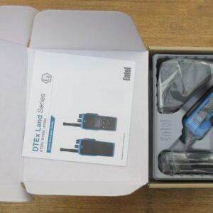 Open box with an Entel DT985 Atex 2c display walkie-talkie, accessories in plastic wrapping, and an instruction manual on a wooden surface.