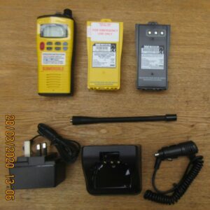 entel-ht649-what-you-get Six electronic accessories for the Entel HT649 Marine VHF GMDSS Emergency Walkie-Talkie, including a yellow submersible radio, two batteries, power adaptor, aerial, charging dock, and car charger on a wooden surface.