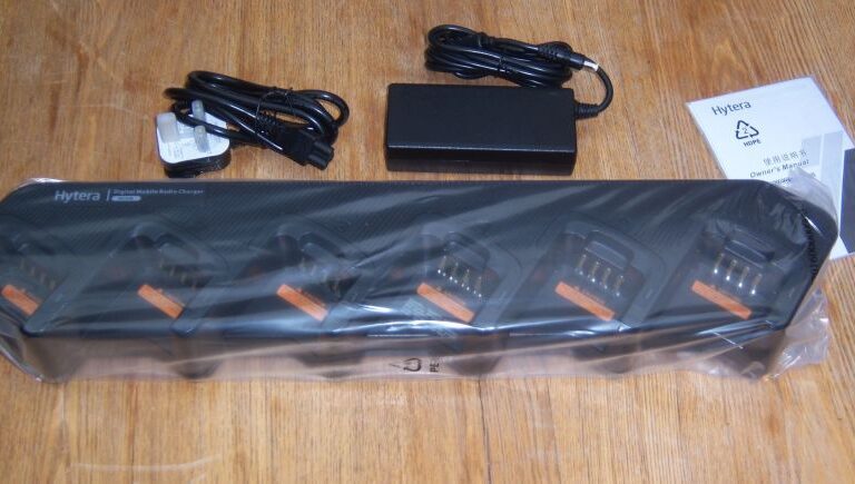 A Hytera PD7xx Battery BL2008/BL2006 multi-unit charger with four slots, power adaptor, cable, and instruction manual displayed on a wooden surface.