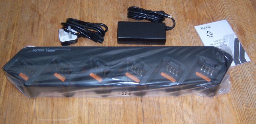  A Hytera PD7xx Battery BL2008/BL2006 multi-unit charger with four slots, power adaptor, cable, and instruction manual displayed on a wooden surface.