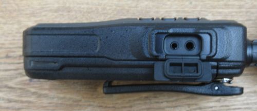 kirisun-dp405-accessory-socket Close-up side view of a Kirisun DP405 Digital / Analogue Walkie-Talkie Radio in black, featuring external accessory ports and a belt clip, resting on a wooden surface.