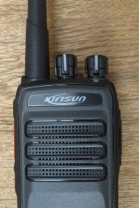 The Kirisun DP405 Digital / Analogue Two-Way Radio, black with an aerial, two control knobs, and speaker grilles, is placed on a wooden surface.