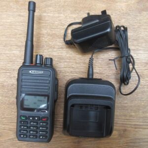 kirisun-dp480-what-you-get A Kirisun DP480 Digital/Analogue Two-Way Radio is shown on a wooden surface with its charging dock and power adaptor.
