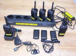 Five Hytera two-way radios with charging stations, batteries, earpieces, and power adaptors arranged on a wooden surface—perfect for Walkie Talkie Radio Hire needs.