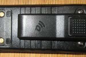 A Quansheng TG330 battery with a black plastic belt clip attached rests on a wooden surface.
