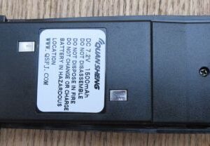 Quansheng TG330 Battery—rectangular and black with a white label listing safety instructions and specifications—rests on a wooden surface.