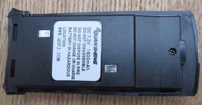 Quansheng TG330 Battery—rectangular and black with a white label listing safety instructions and specifications—rests on a wooden surface.