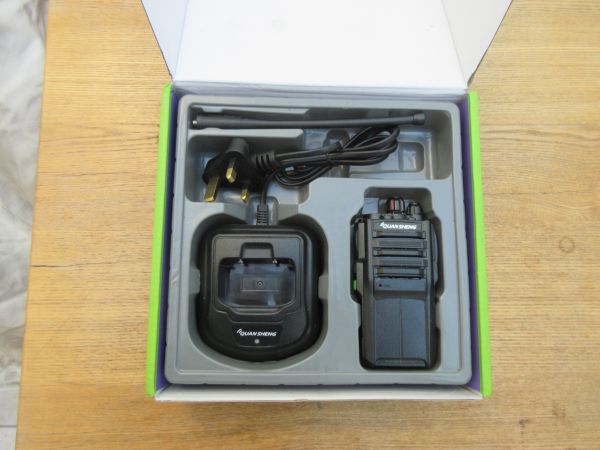 quansheng-tg330-walkie-talkie-box-contents Box containing a Quansheng TG330 Walkie Talkie Radio, charging dock, plug, and aerial neatly arranged in moulded packaging on a wooden surface.