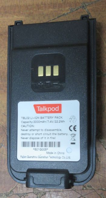talkpod-a50p-battery A standard battery for Talkpod A50P radios, showing its label with 3000mAh capacity, 7.4V voltage, 22.2Wh energy rating, and safety warnings, rests on a wooden surface.