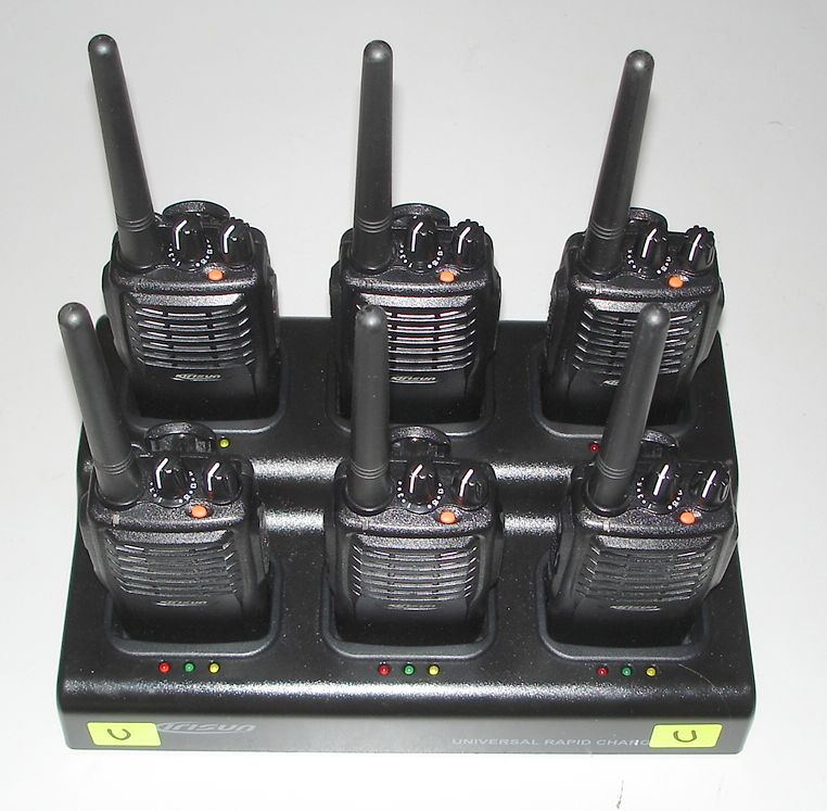 Six walkie-talkies are placed in a black charging station with indicator lights on each slot, arranged in two rows of three.